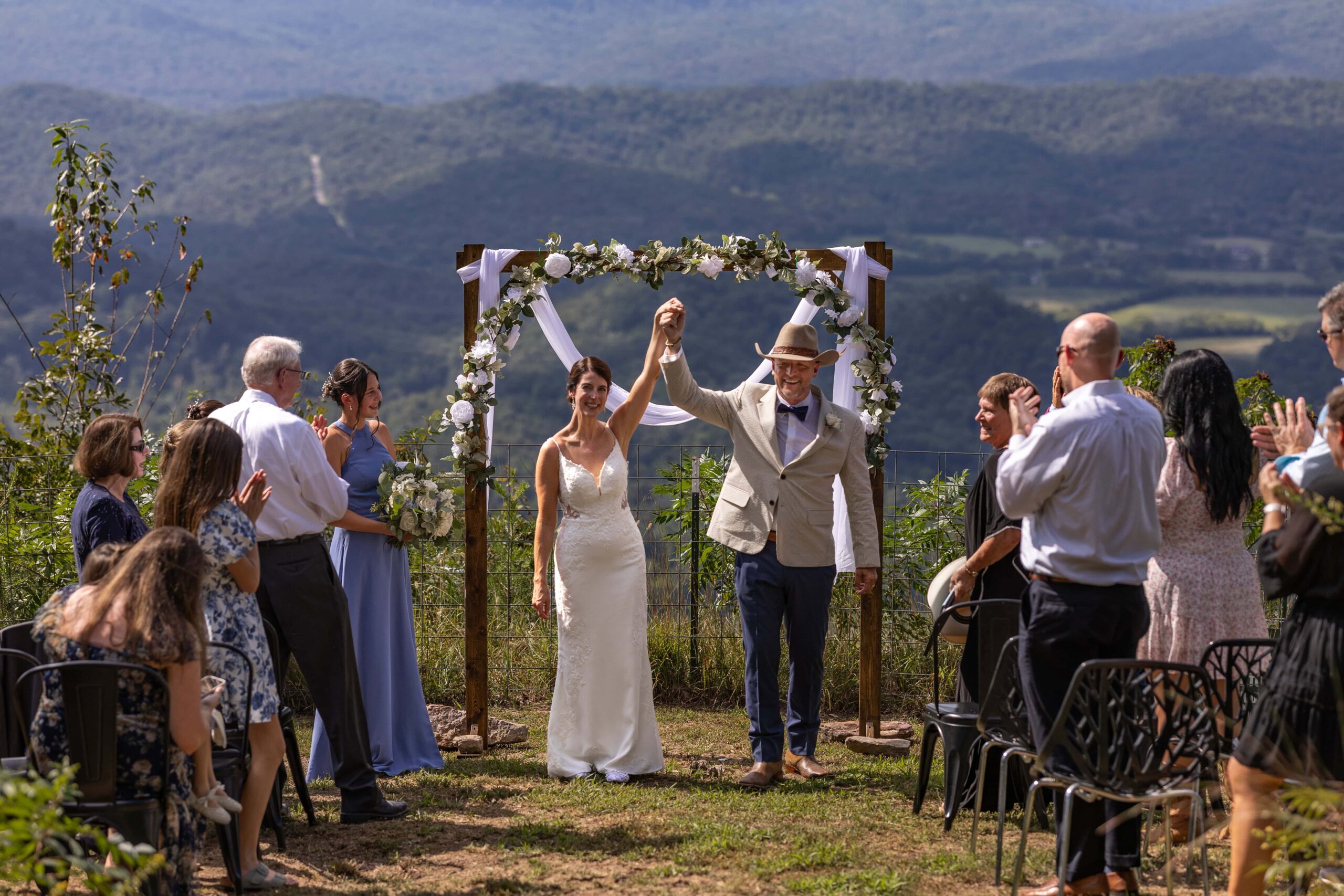 A bride and groom stand at the front of a crowd smiling with their arms in the air after eloping with family. They are eloping in Georgia at Lookout Mountain.