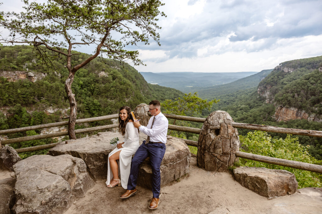 A groom is signing a marriage license after eloping in Georgia. They are sitting on a large rock in front of a mountain view. The groom is using the brides back as a sturdy surface to sign the marriage license on.