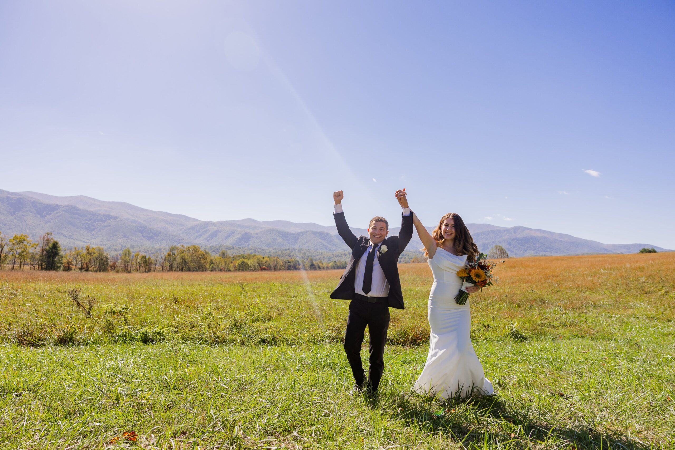 A bride and groom are walking side-by-side holding their hands in the air, smiling, and cheering after their elopement. They are so happy their elopement planning paid off and they are living their dream elopement day.