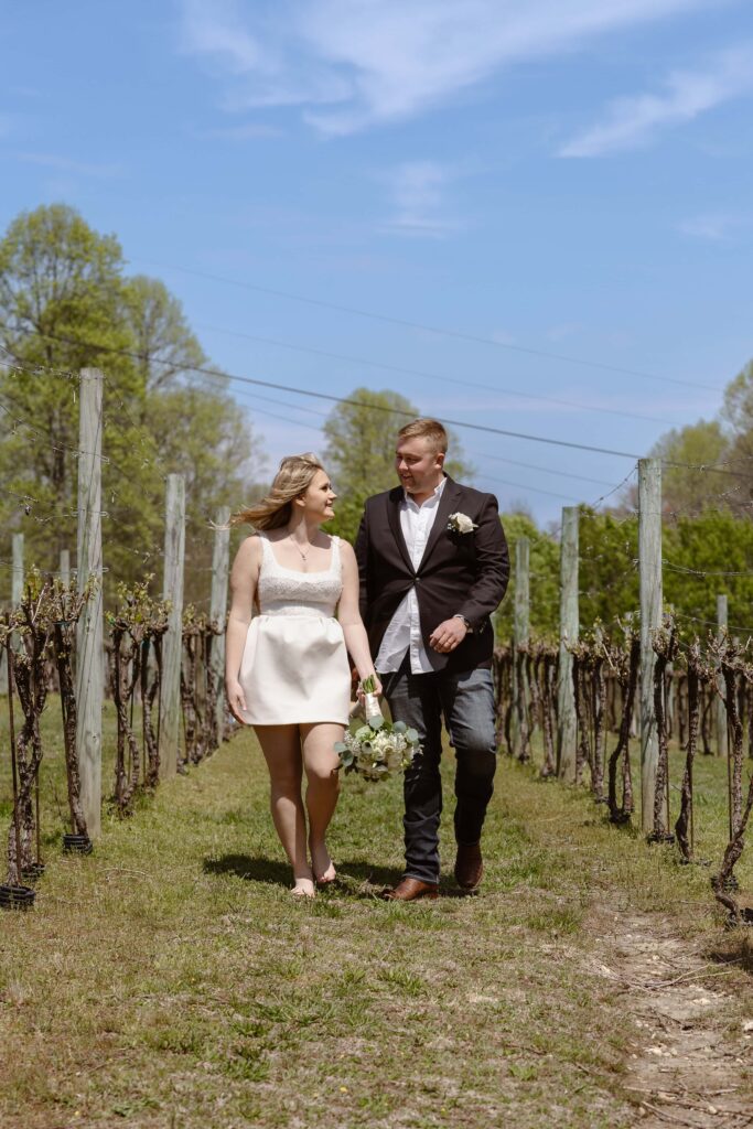 A bride and groom stroll through a vineyard enjoying the sunshine and warm weather after eloping.