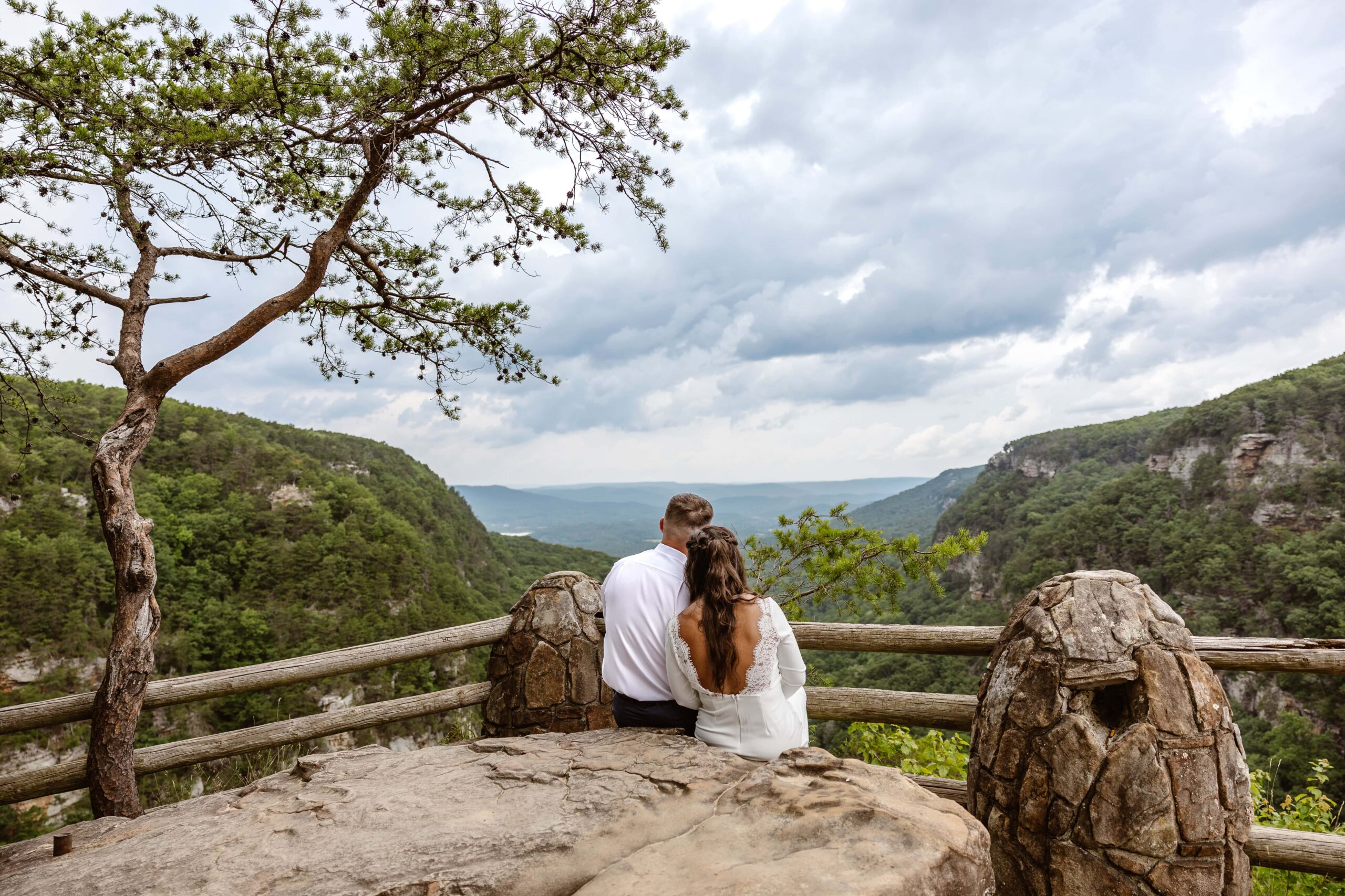 A bride and groom sit side by side with their backs facing the camera looking out at a mountain view after eloping. The brides head is gently resting on the groom shoulder.