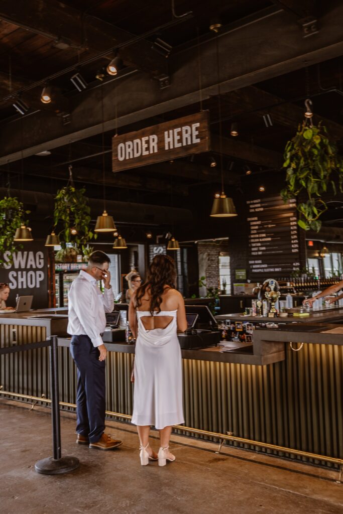 A bride and groom stand with their backs facing the camera. They are at a bar of a local Chattanooga Brewery ordering beers on their elopement day.