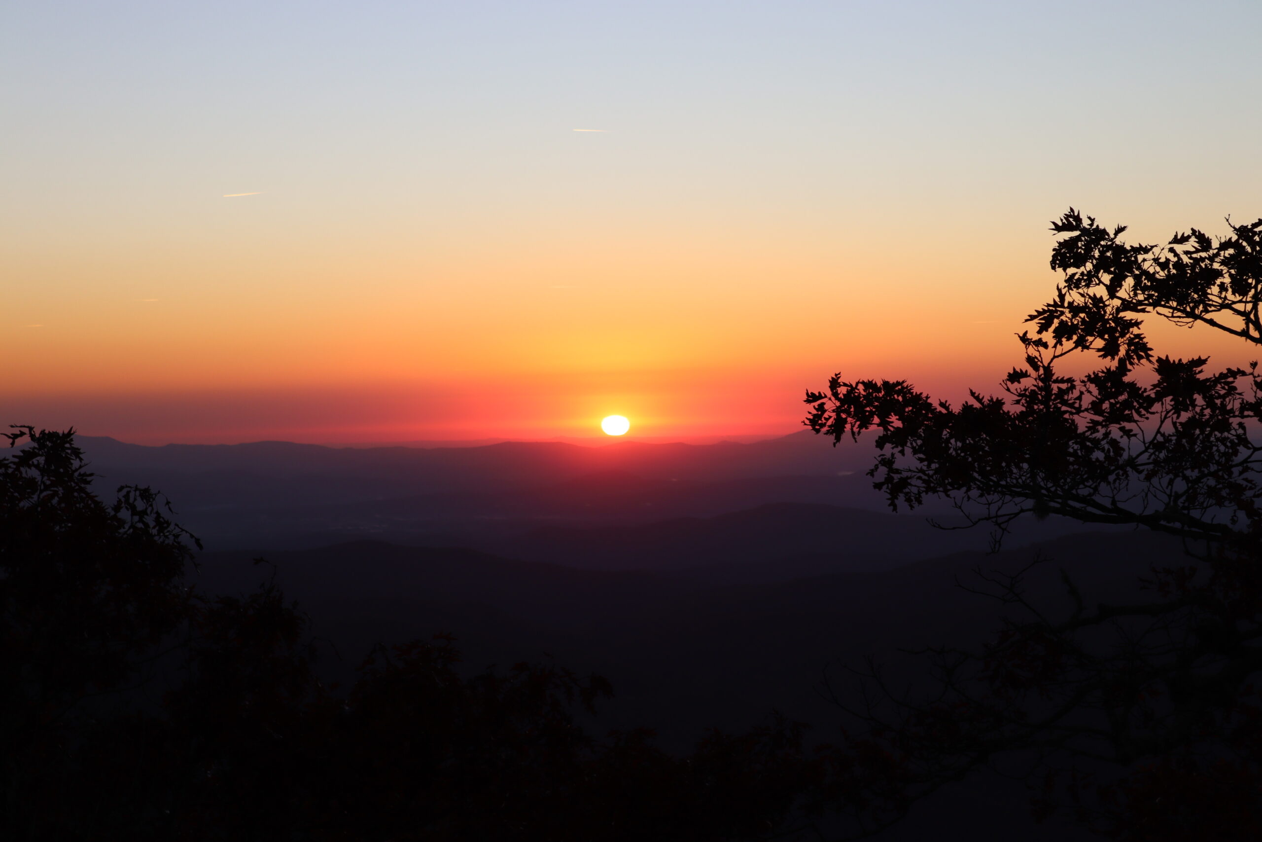The sun is rising over the Blue Ridge mountains. The sky is shades of blue, orange, pink and red. The mountains are a hue of blue. This is the perfect backdrop for a Blue Ridge Elopement