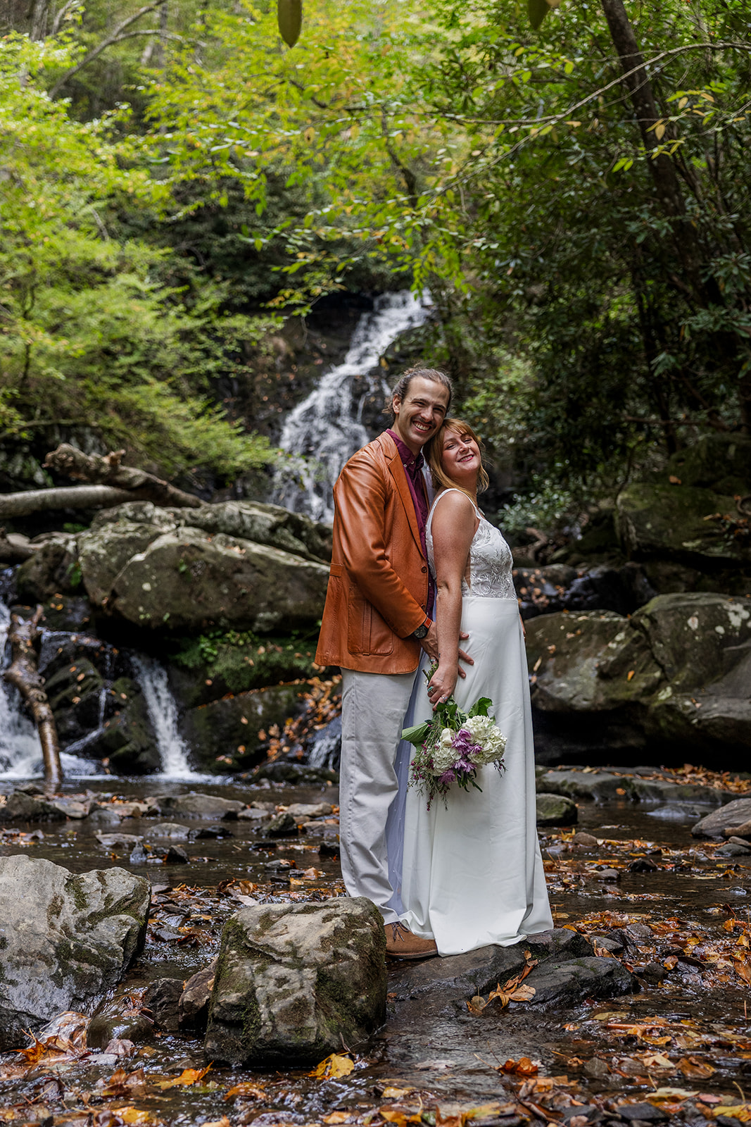 bride and groom pose below a waterfall in a steam