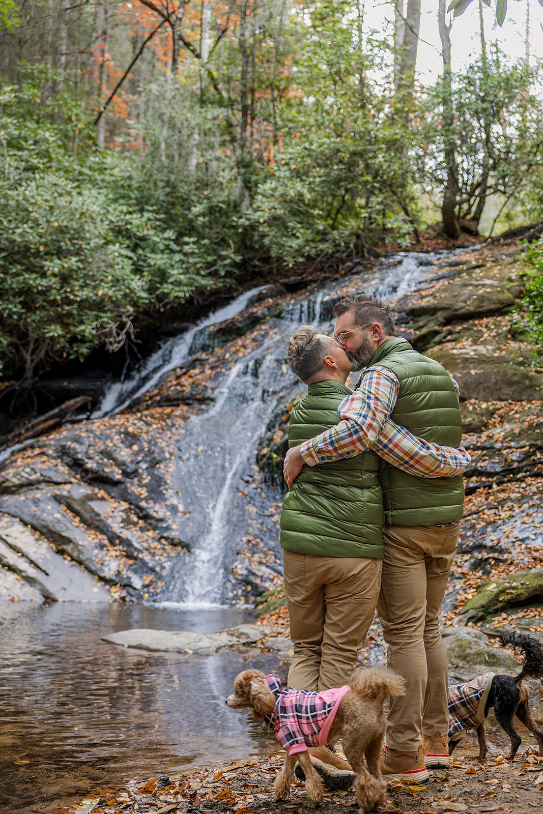 couple share a kiss with their dogs by the streams edge