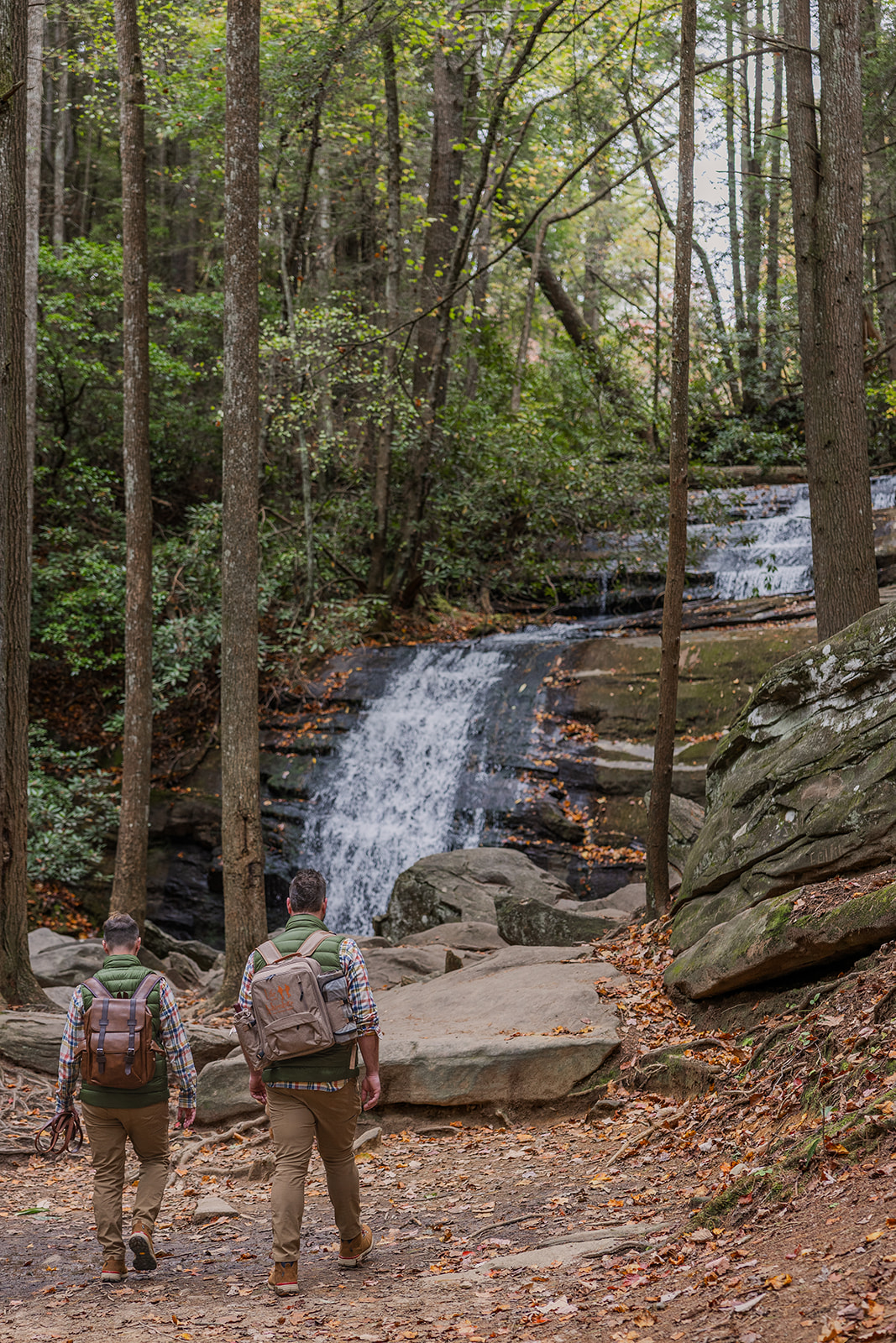 gay couple walk to the waterfall to begin their waterfall elopement