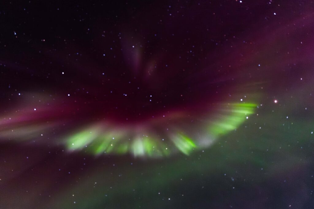 A burst or pink and green hues of Northern lights contrast the dark starry sky.