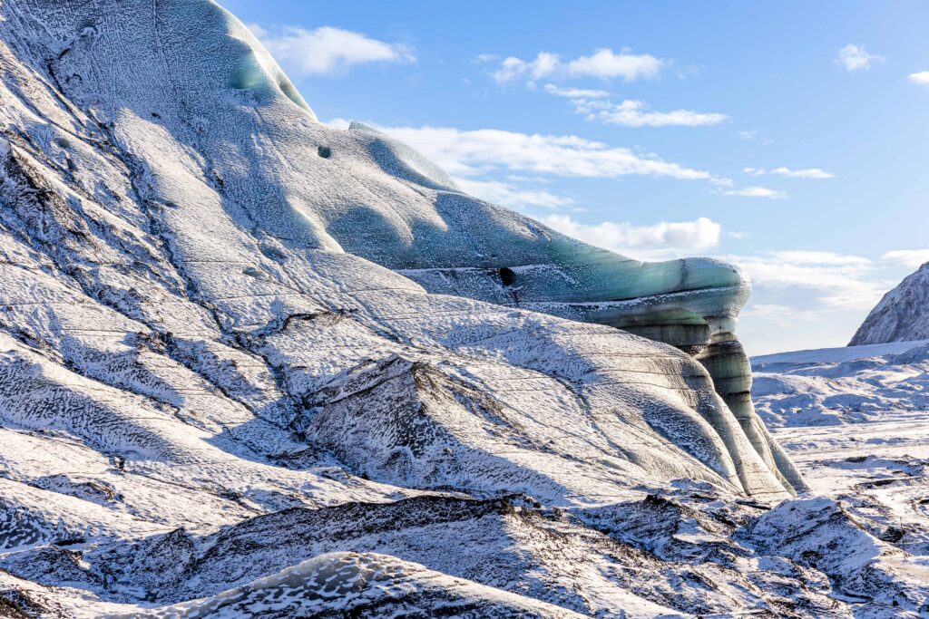 A snow covered glacier is pictured. The glacier is cascading over a large area with various shades of black, white and blue.