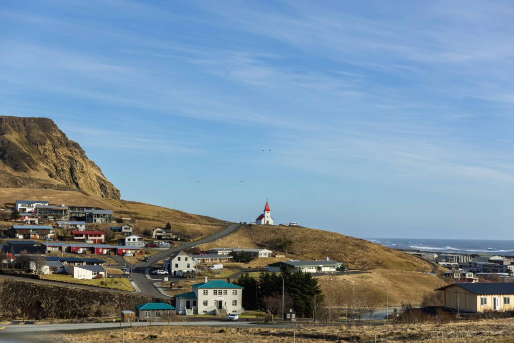 A white and red church sits atop a mossy mountain top overlooking houses and the sea. If you are wondering where to elope in Iceland, this is a great spot.