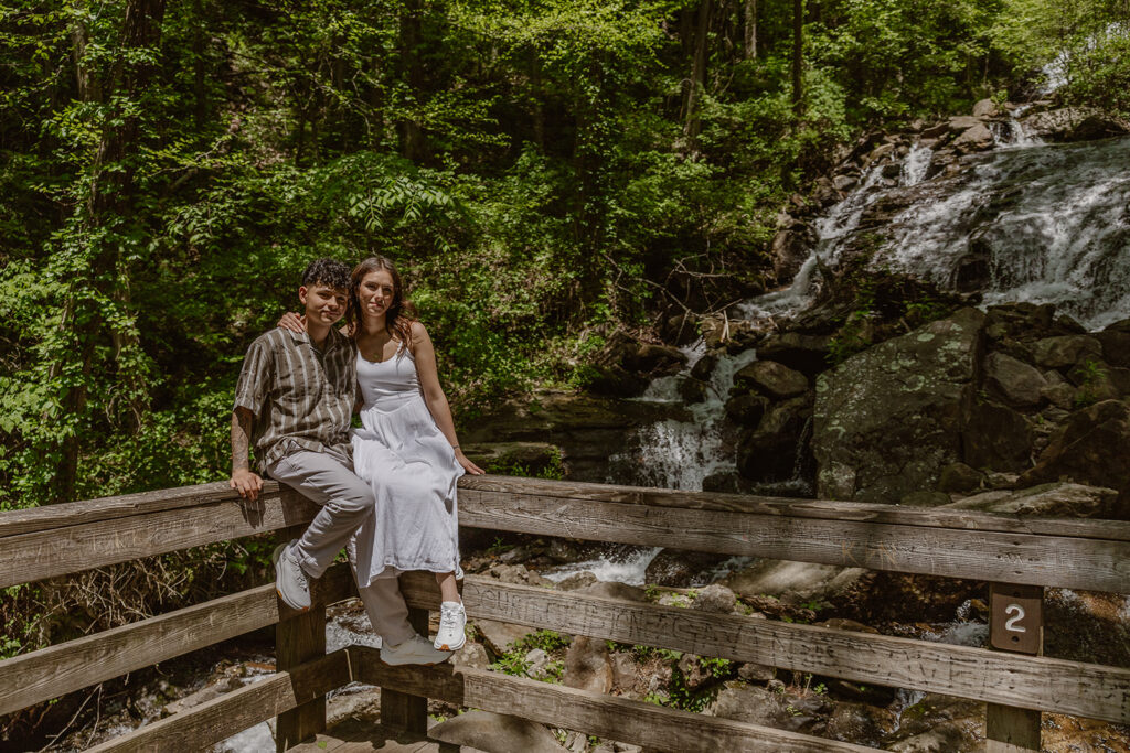 bride and groom sit on the fence with a waterfall in the background