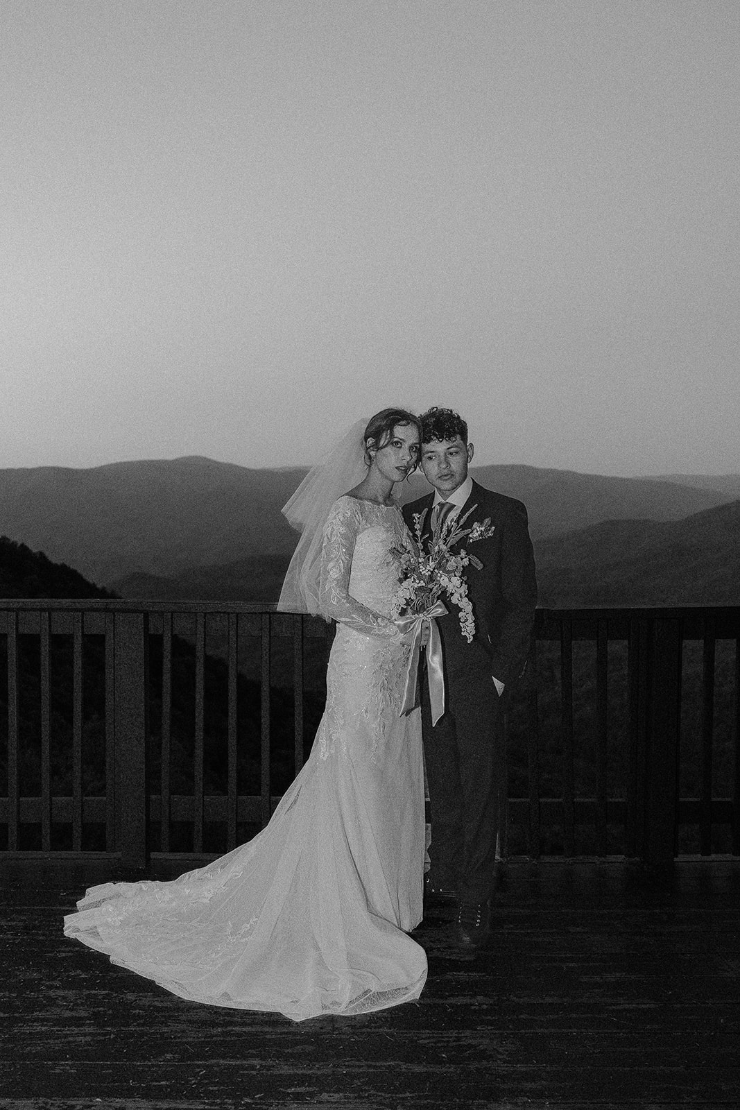 beautiful bride and groom pose on the balcony overlooking the mountains 