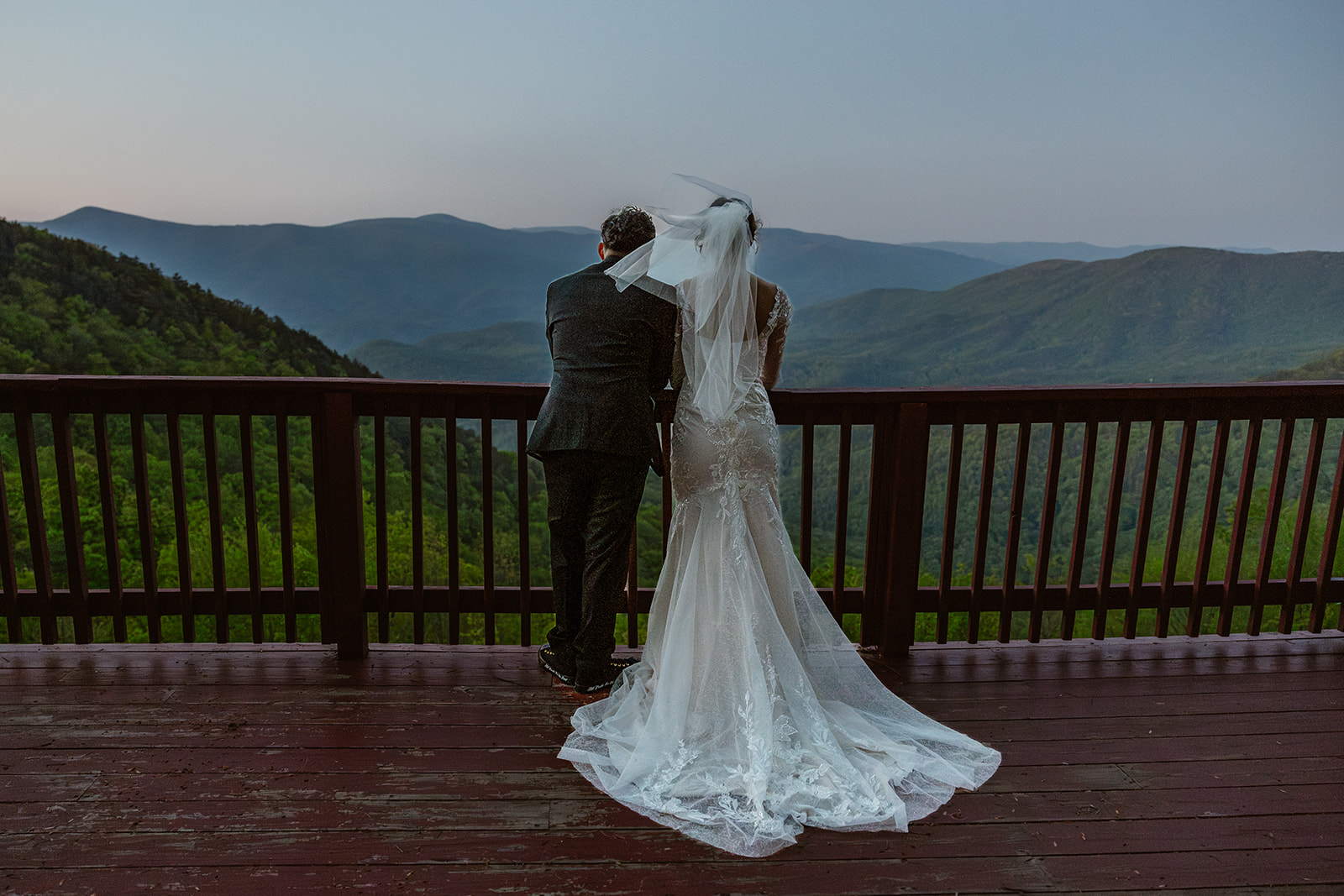 beautiful bride and groom pose on the balcony overlooking the mountains 