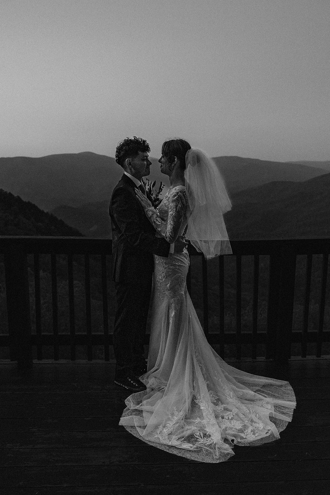 beautiful bride and groom pose on the balcony overlooking the mountains 