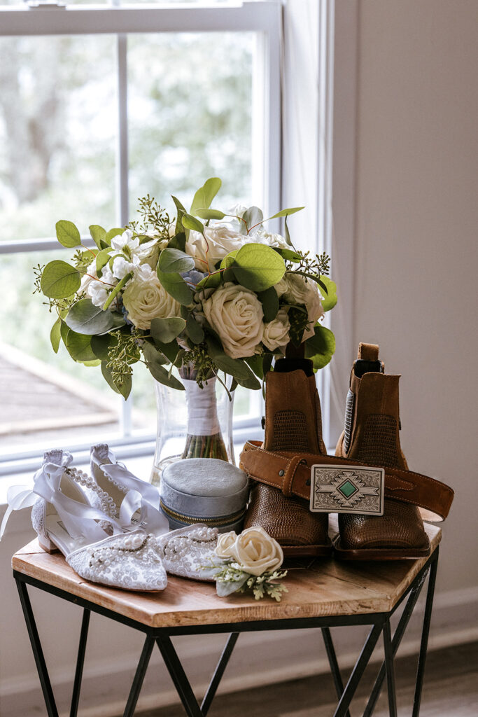 A bride and grooms elopement shoes sit on a table waiting for them to dress There also is a bouquet, and accessories ready for their elopement day