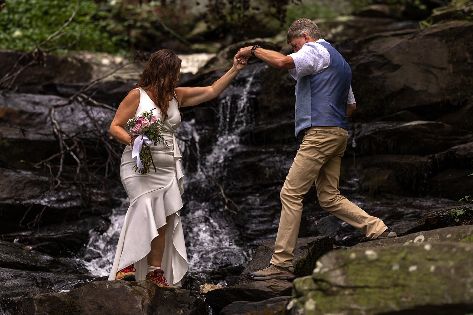 bride and groom hiking through a waterfall together