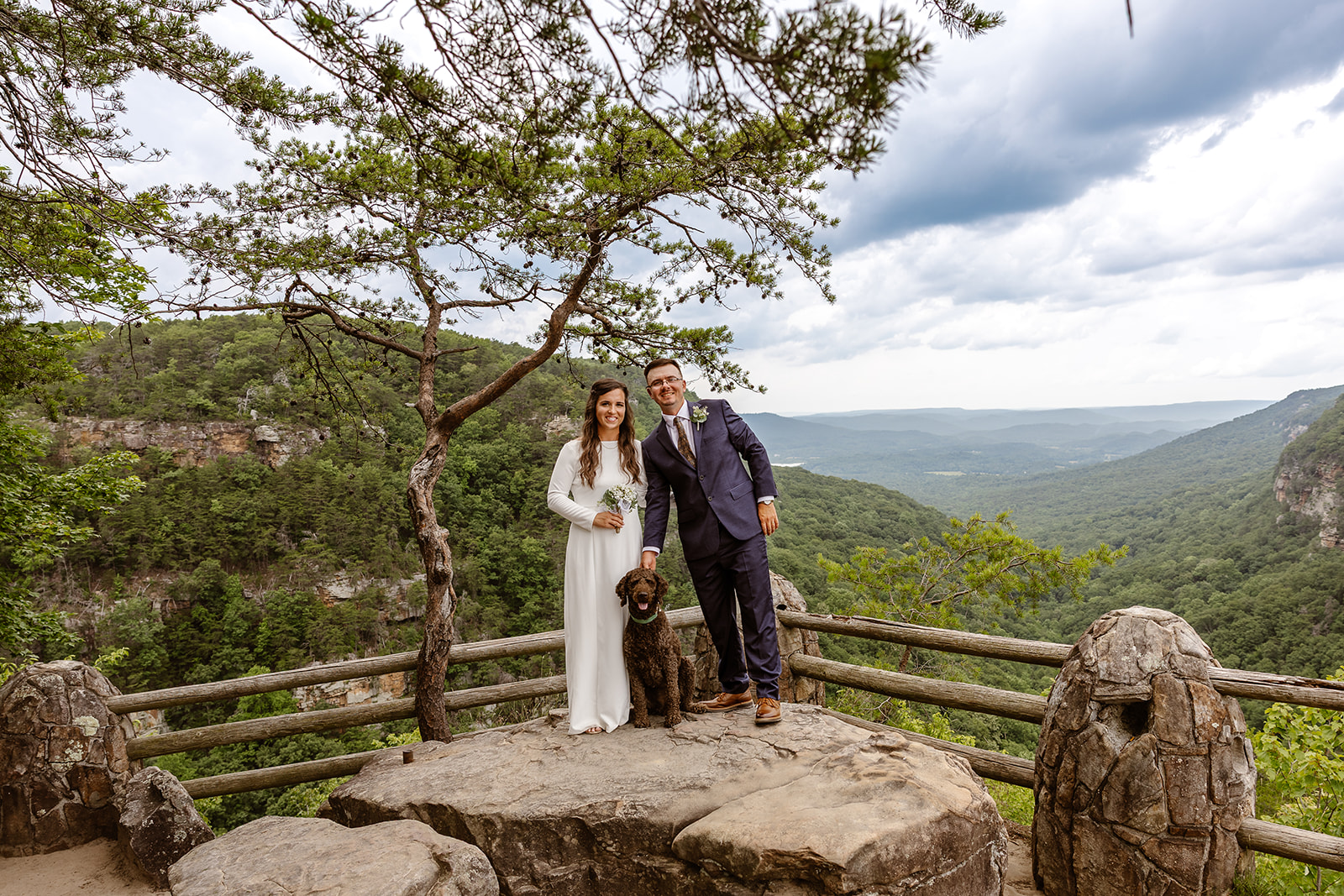 bride and groom pose with their dog as the mountains stretch in the background
