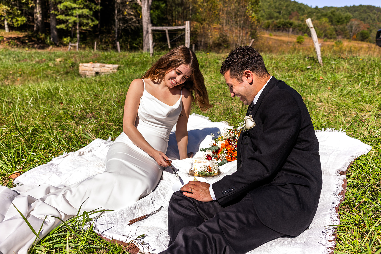 stunning wedding cake sits on the picnic blanket with the bride and groom